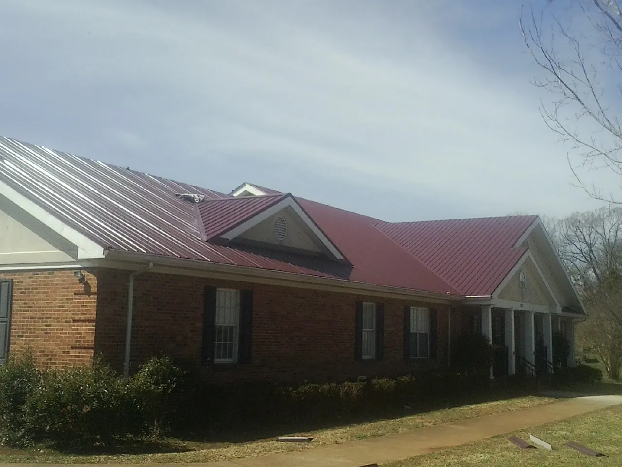 Red metal roof with gabled entries on a long brick building, from a Hail Damage Roof Repair job in New London
