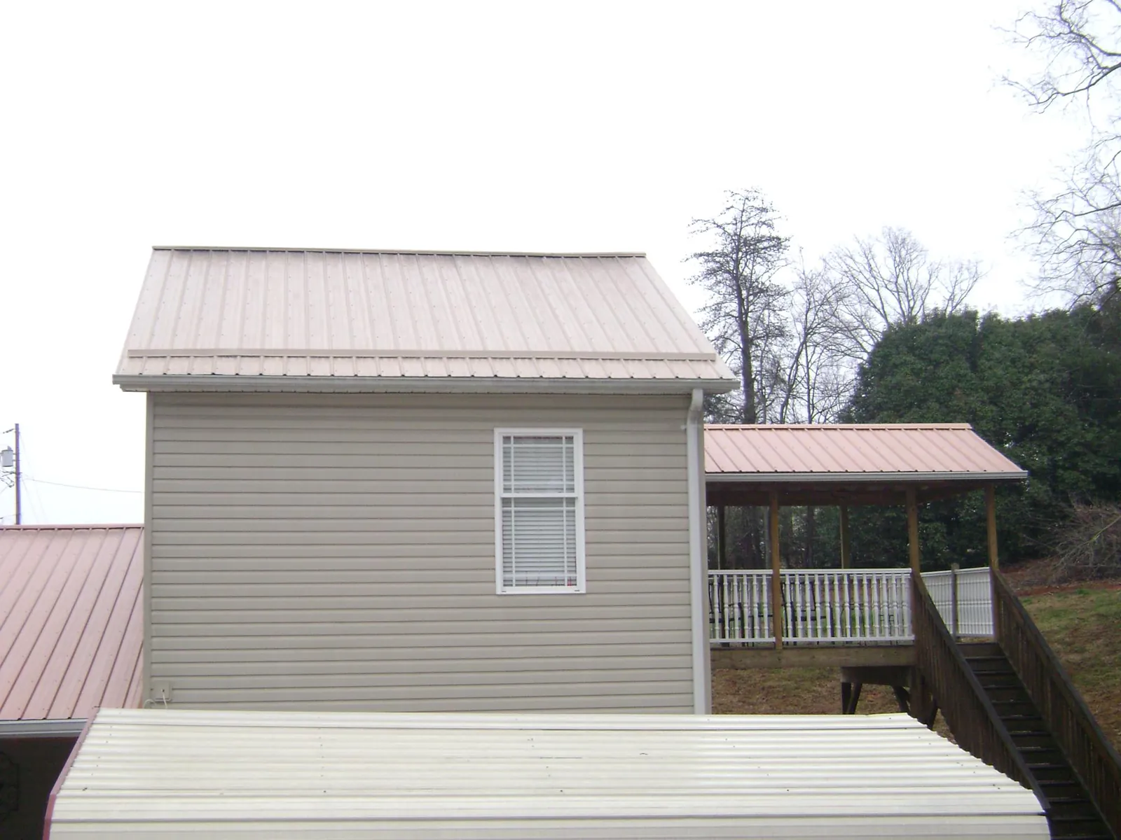 Tan metal roofs on a two story addition and attached porch, from a Roof Replacement job in New London